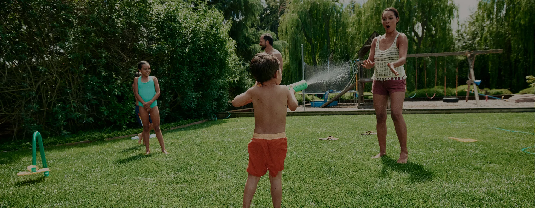 Parents and their two children playing in the backyard with squirt guns
