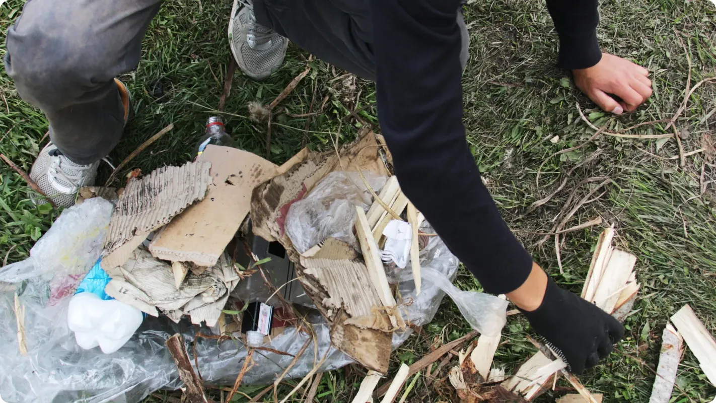 A person cleaning up cardboard trash and yard debris from a outdoor grass lawn to clear pest nesting sites.