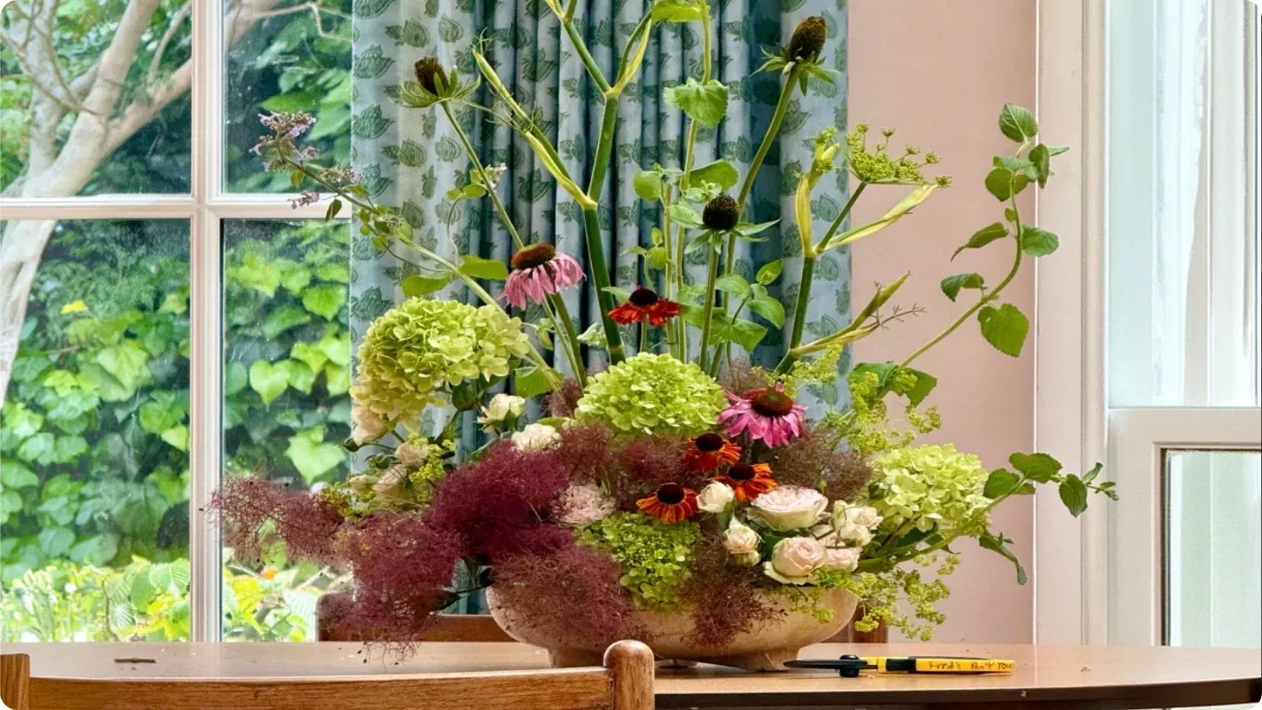 Floral arrangement with hydrangeas, purple coneflowers, and smoke bush foliage on a wooden table.