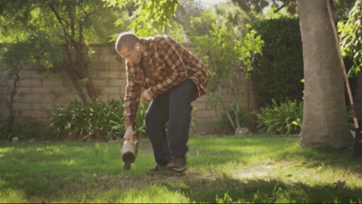 Person raking soil in a bare lawn patch next to a container of Scotts EZ Seed grass seed.