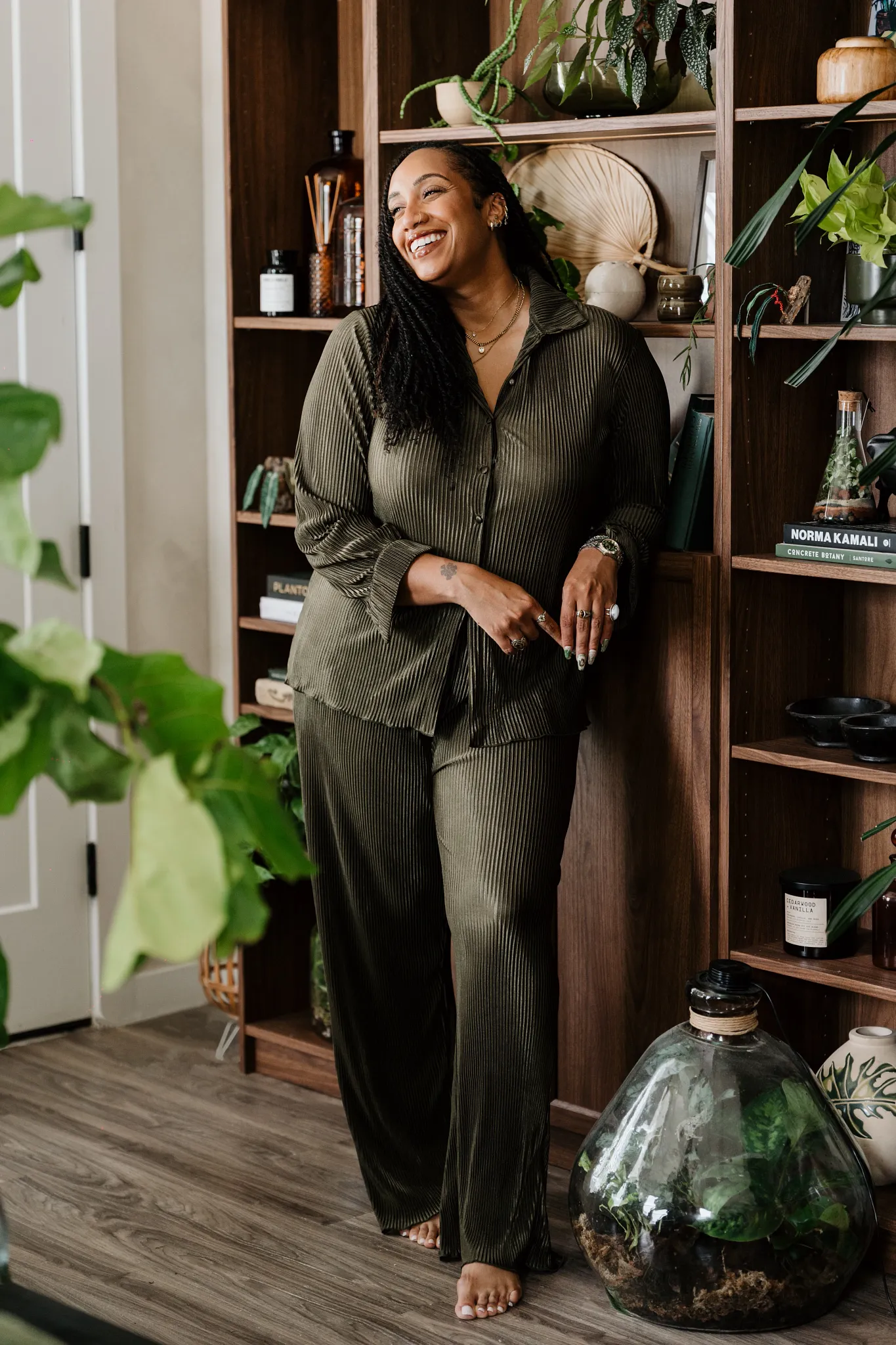 Britt standing in front of a her bookcase that has plants on almost every shelf.