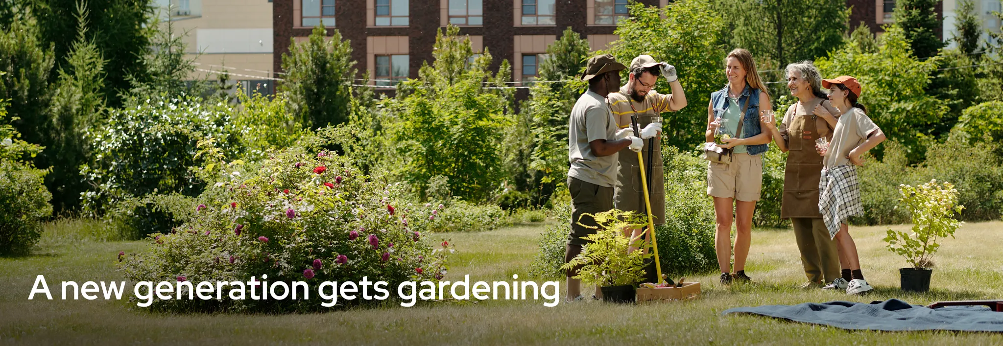 A group of people from different generations standing together in a sunny community garden, enjoying refreshing drinks and chatting near flowering bushes and potted plants.