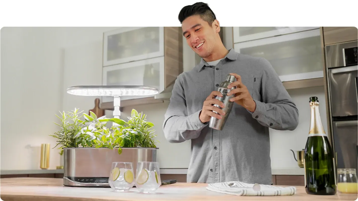 A man using a drink shaker near an indoor countertop hydroponic herb garden for making fresh cocktails.