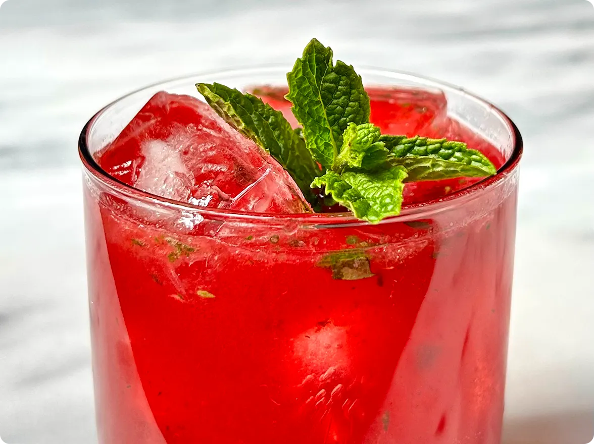 Text listing five fresh mint recipes including Sicilian-Inspired Pesto, Cherry Bourbon Smash cocktail, Faux-toush Salad, Ginger Mint Bellini, and Italian Salsa Verde, shown alongside a close-up image of a vibrant red iced cocktail served in a glass and garnished with fresh green mint leaves.