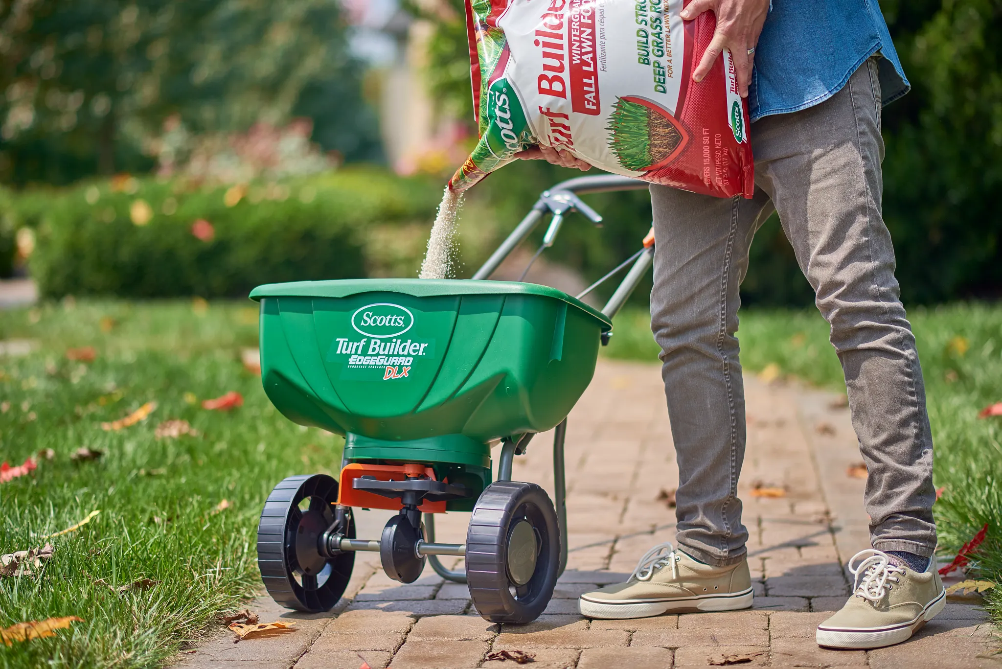 Person pouring Turf Builder WinterGuard Fall Lawn Food into a Scotts DLX Broadcast spreader