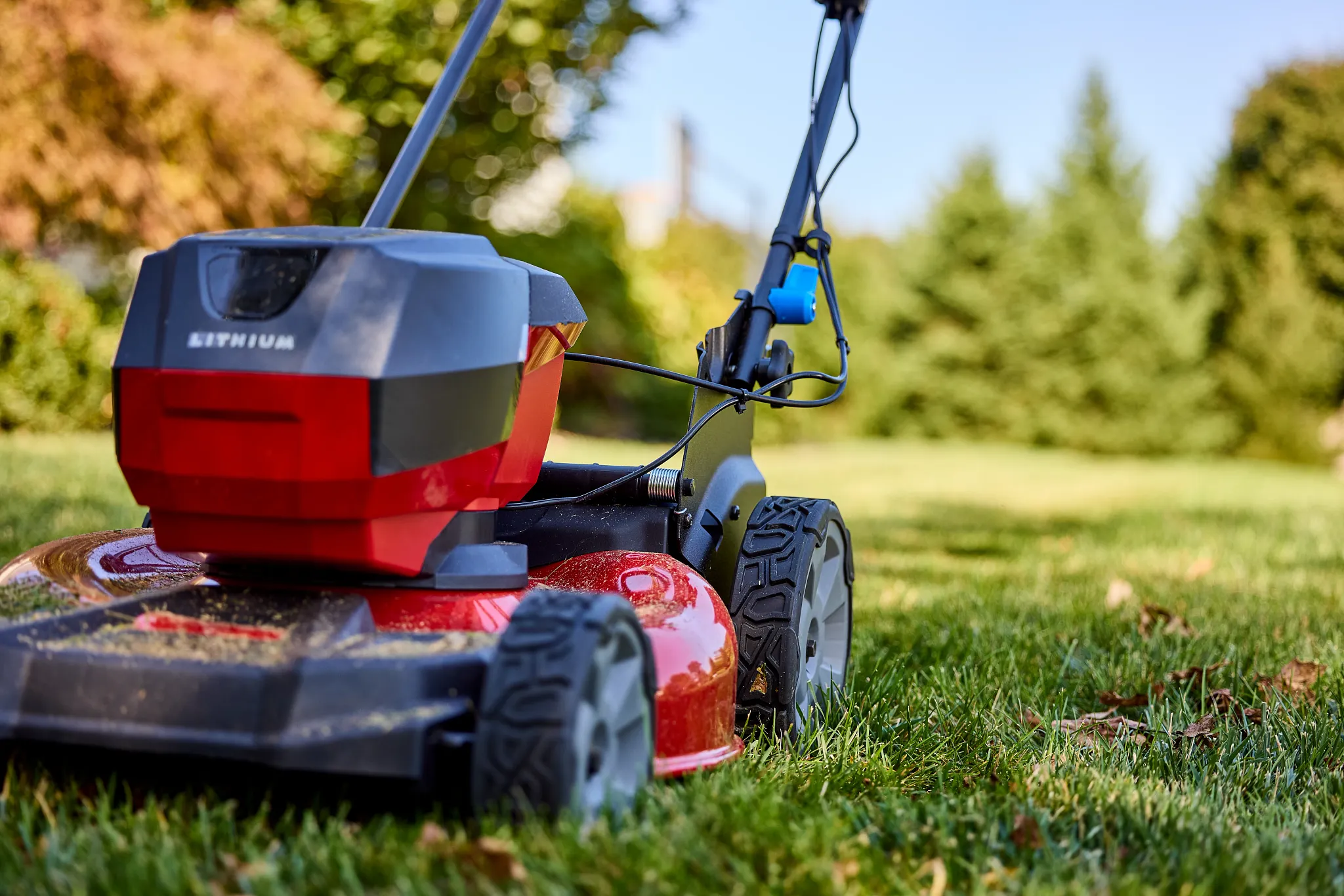 A red and black lawn mower sits on a green lawn, with trees in the background.