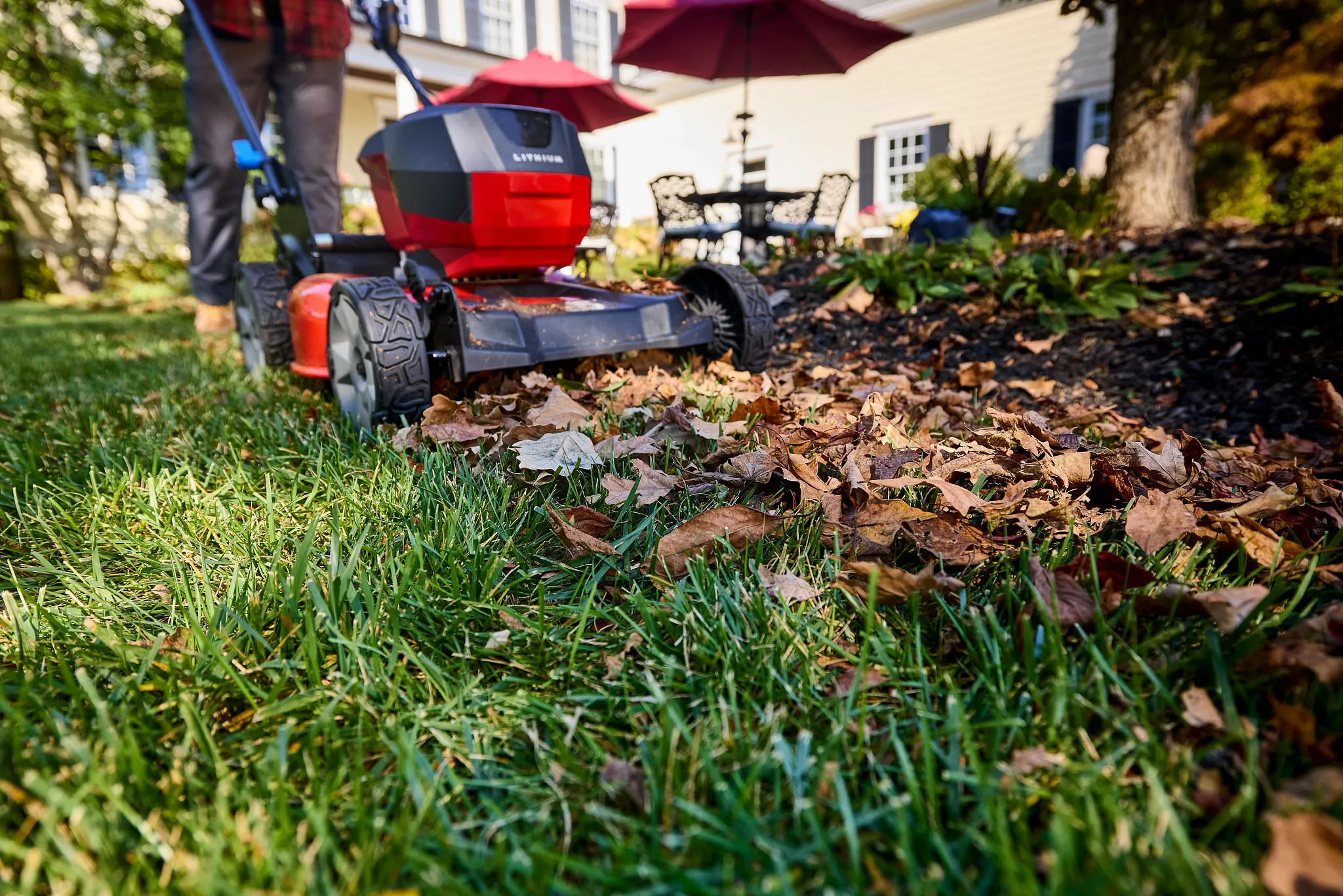 A low-angle shot of a lawn mower mulching a large pile of fallen leaves.