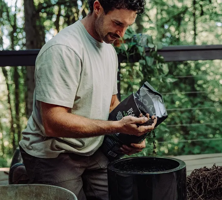Person holding a bag of Black Magic Potting Soil in one hand and raw soil in the other hand.
