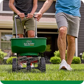 a dad showing his son how to use a turf builder spreader on the lawn