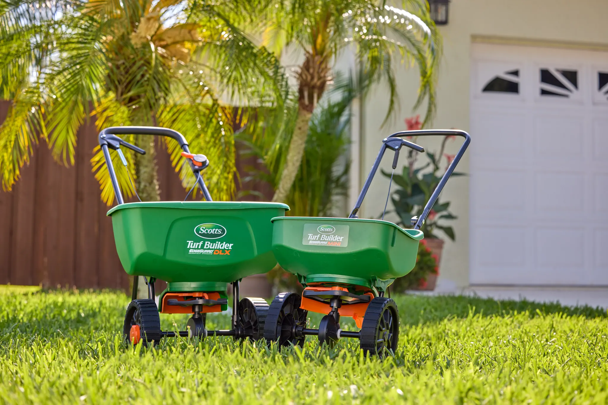 A Scotts DLX and Mini broadcast spreader positioned side-by-side in a lawn.