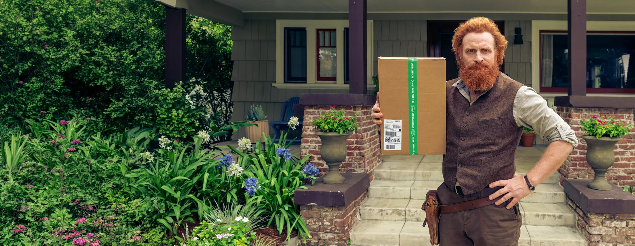 Scottie standing on the front steps of a brick house with a shipping box  from Scotts with his subscription lawn food