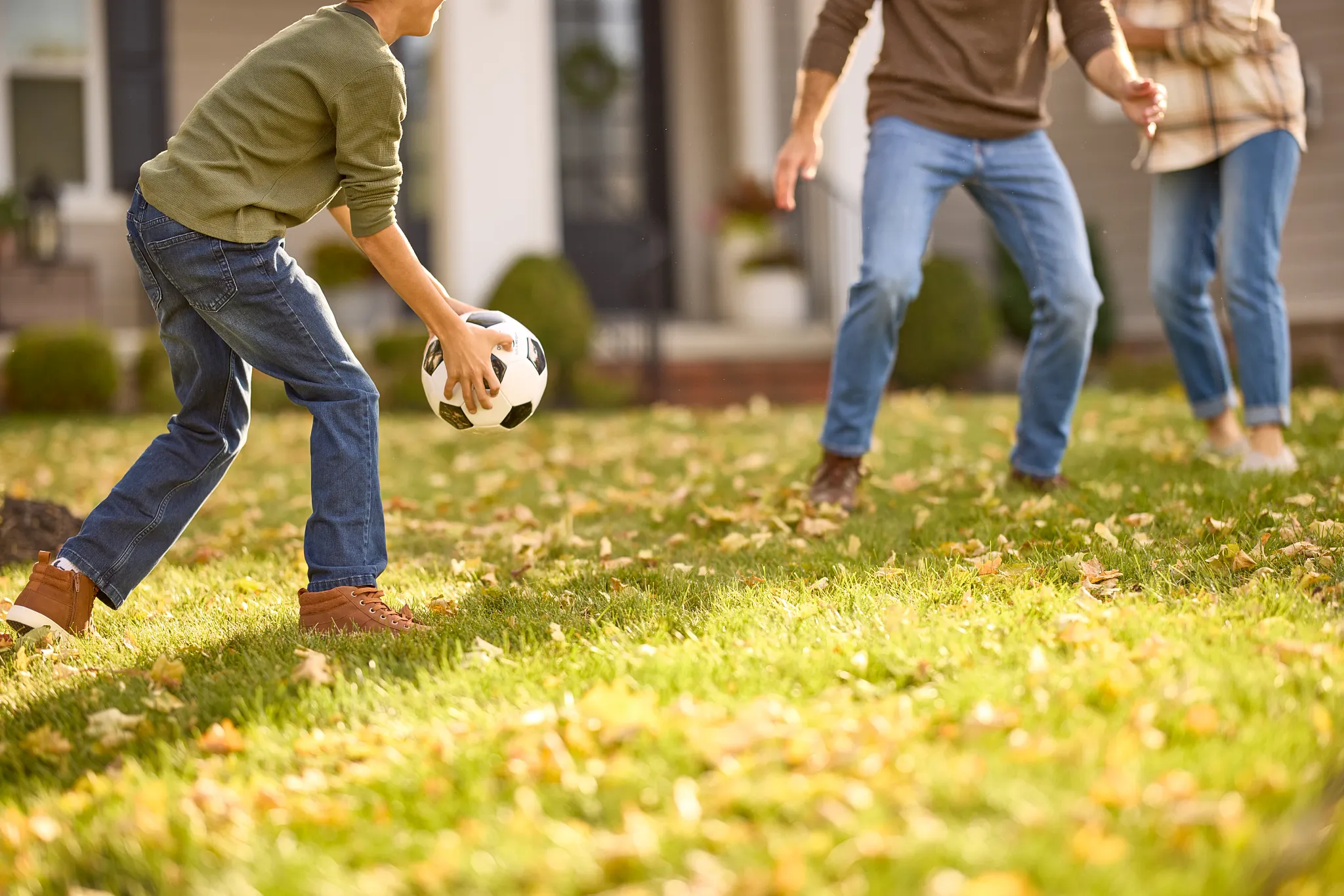 Family playing soccer in fall on a lawn covered with leaves