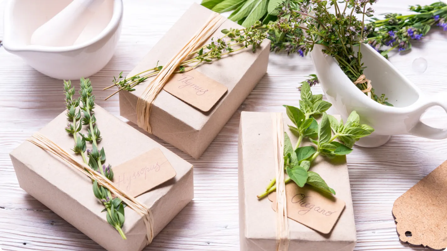 gifts wrapped in light brown kraft paper tied with twine and using snips of herbs as an accent to the tie on the packaging