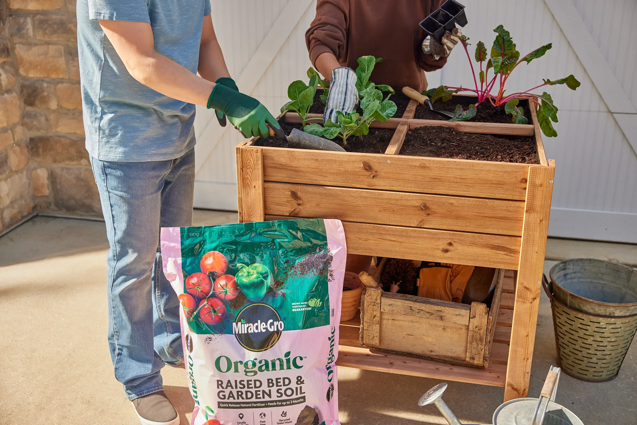 Two people plant an organic garden with fall vegetables with a bag of Miracle-Gro Organic soil sits in front of the elevated raised bed.