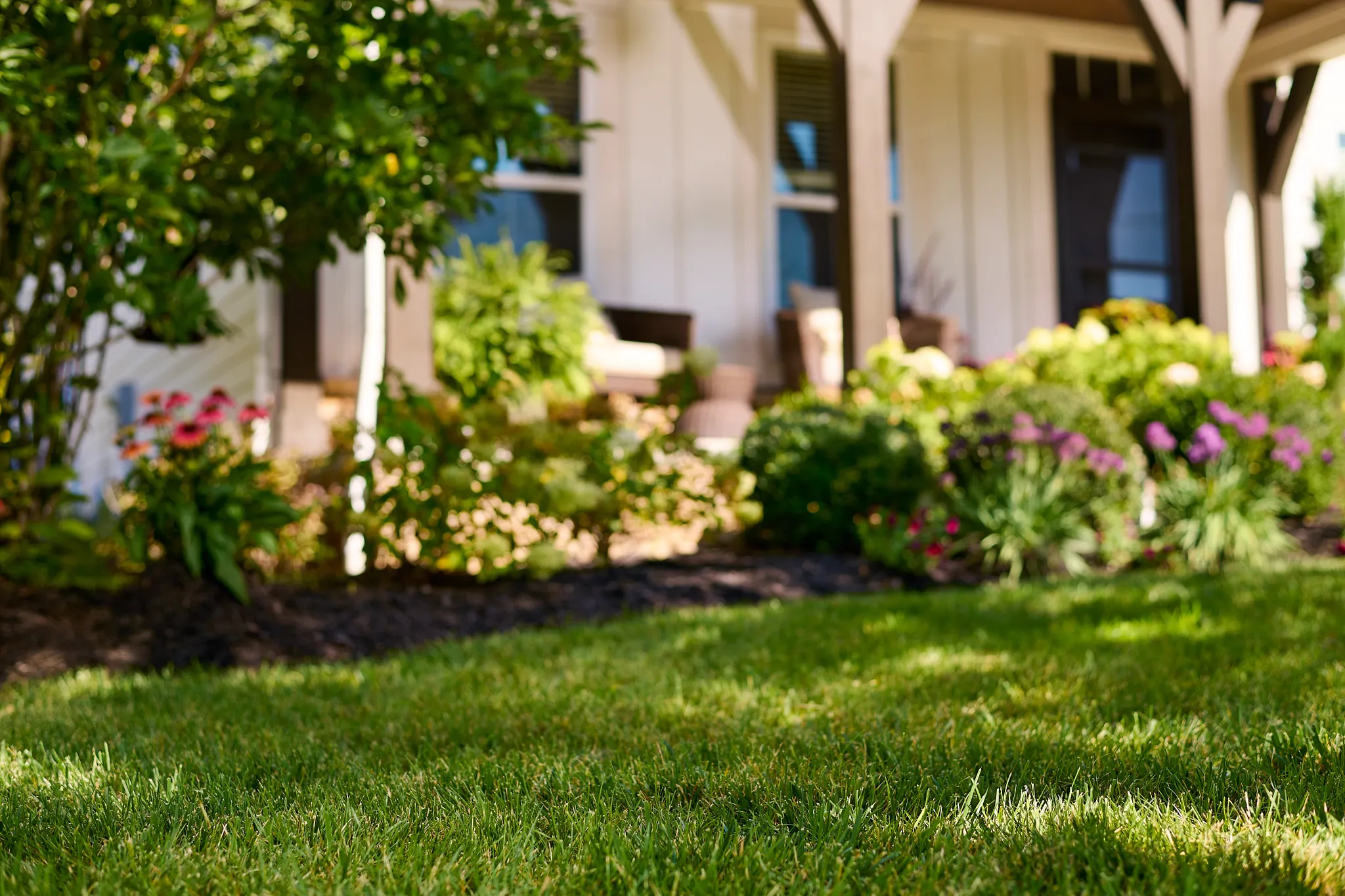 Summer view of a front porch with perennial garden in full bloom and green grass lawn