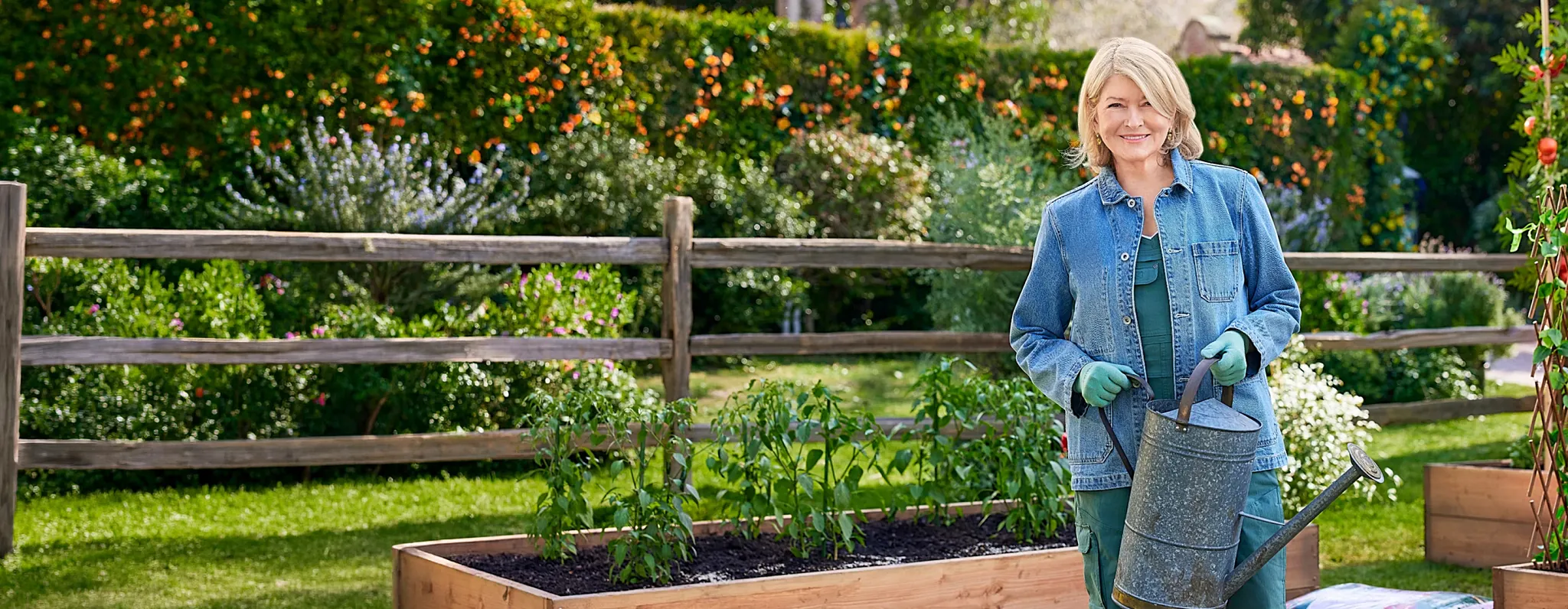 Martha Stewart standing in her garden holding a metal watering can
