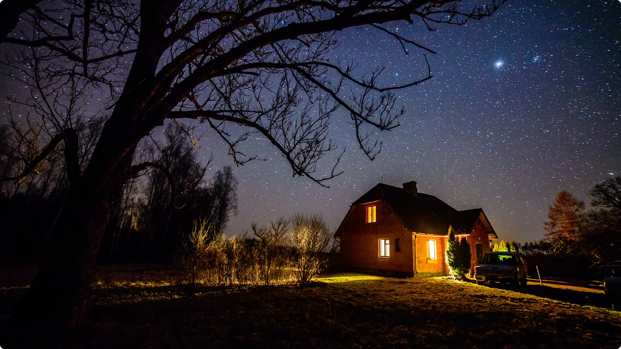 Text reflection on the beauty and peace of rural nightfall and star-filled skies, accompanied by a nighttime photo of a warm-lit brick home, parked SUV, and glowing fireflies in a grassy yard under a dense field of stars.