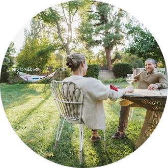 two people sitting at table in yard with hammock in background