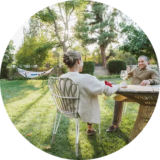 two people sitting at table in yard with hammock in background