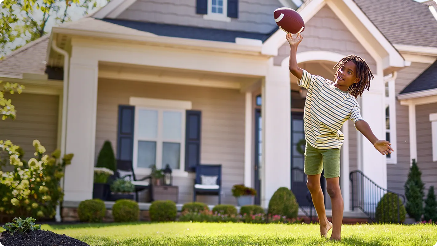 little boy playing catch with a football in bare feet on the front lawn