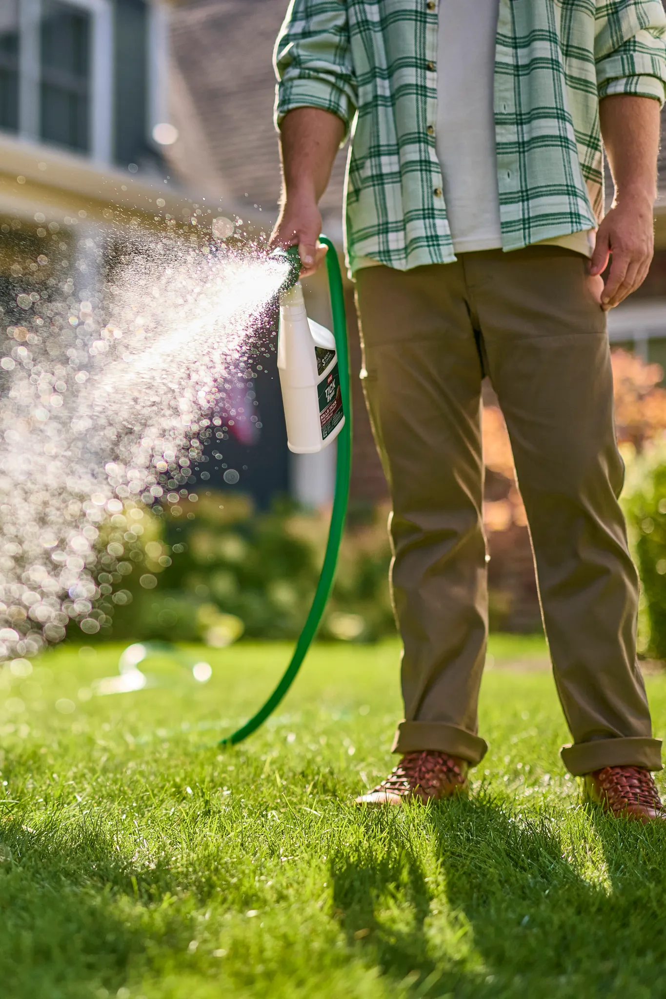 Homeowner applying tick spray to yard using a hose-end sprayer to treat lawn and garden borders for tick control