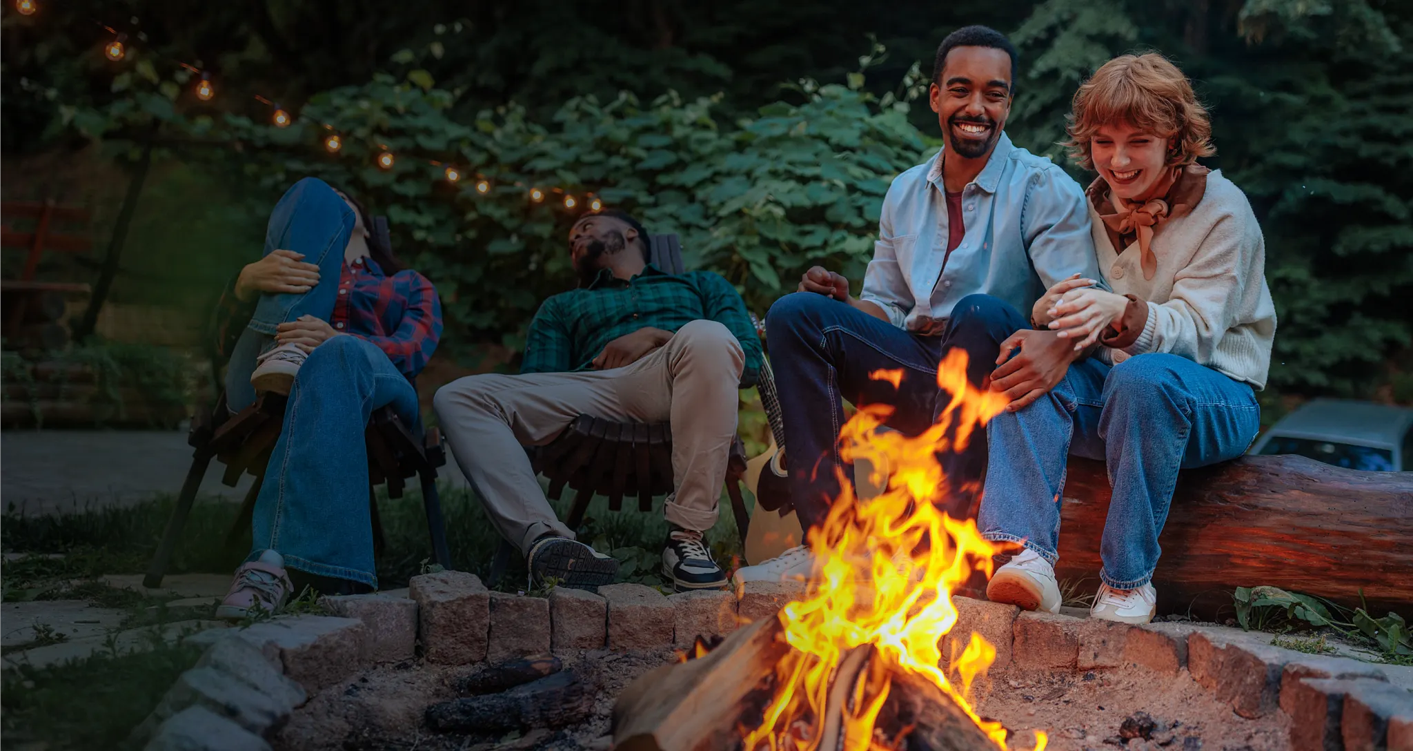 A high-angle lifestyle photograph of two people sitting outdoors on a wooden bench around a brick fire pit with burning orange flames and smoke. Text on the left side reads, "The surprising science of backyard bonfires or, the secret power of backyard bonfires or, are humans hardwired to love bonfires?" followed by body paragraph copy detailing research on backyard rituals and a byline reading "By: Alison Weintraub." A purple circular icon containing a white letter "C" is overlaid in the upper center of the image.