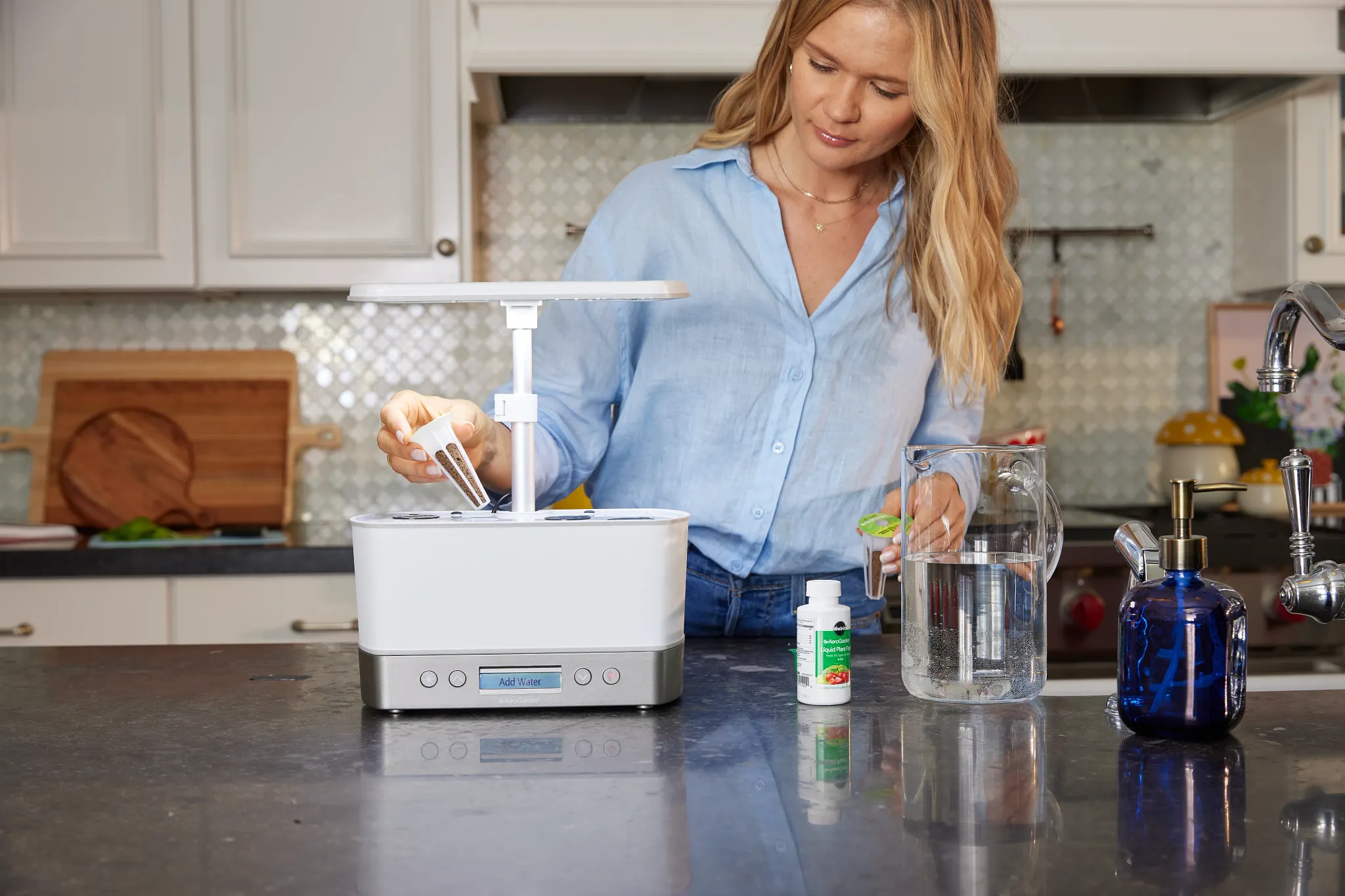 Woman in long-sleeve light blue button down shirt adds pre-seeded seed pods to her AeroGarden unit.