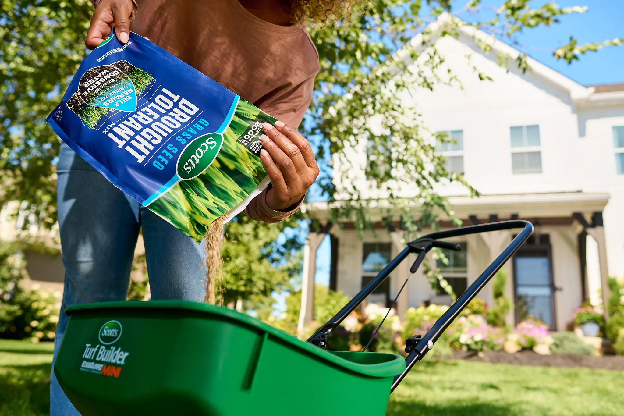 Woman pouring Drought Tolerant Mix grass seed into a Mini spreader.