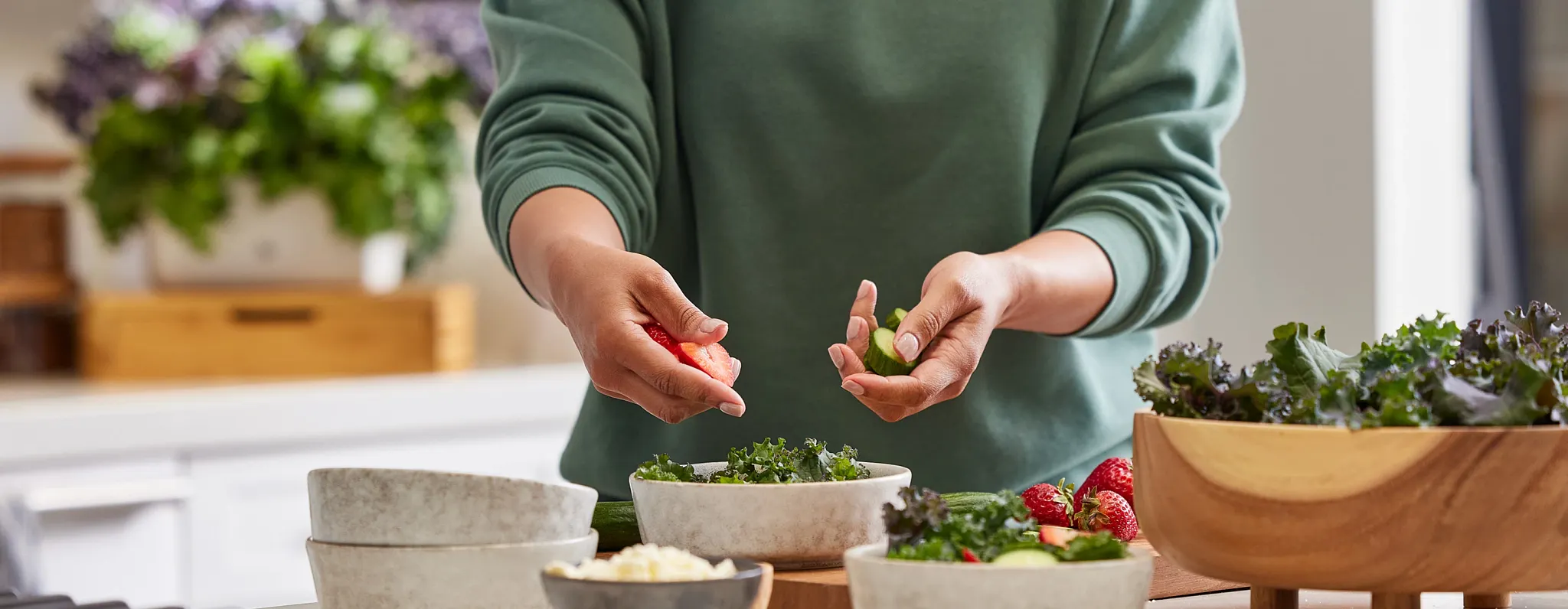 A person tossing fresh garden salad in ceramic bowls on a counter for healthy home-grown meals.
