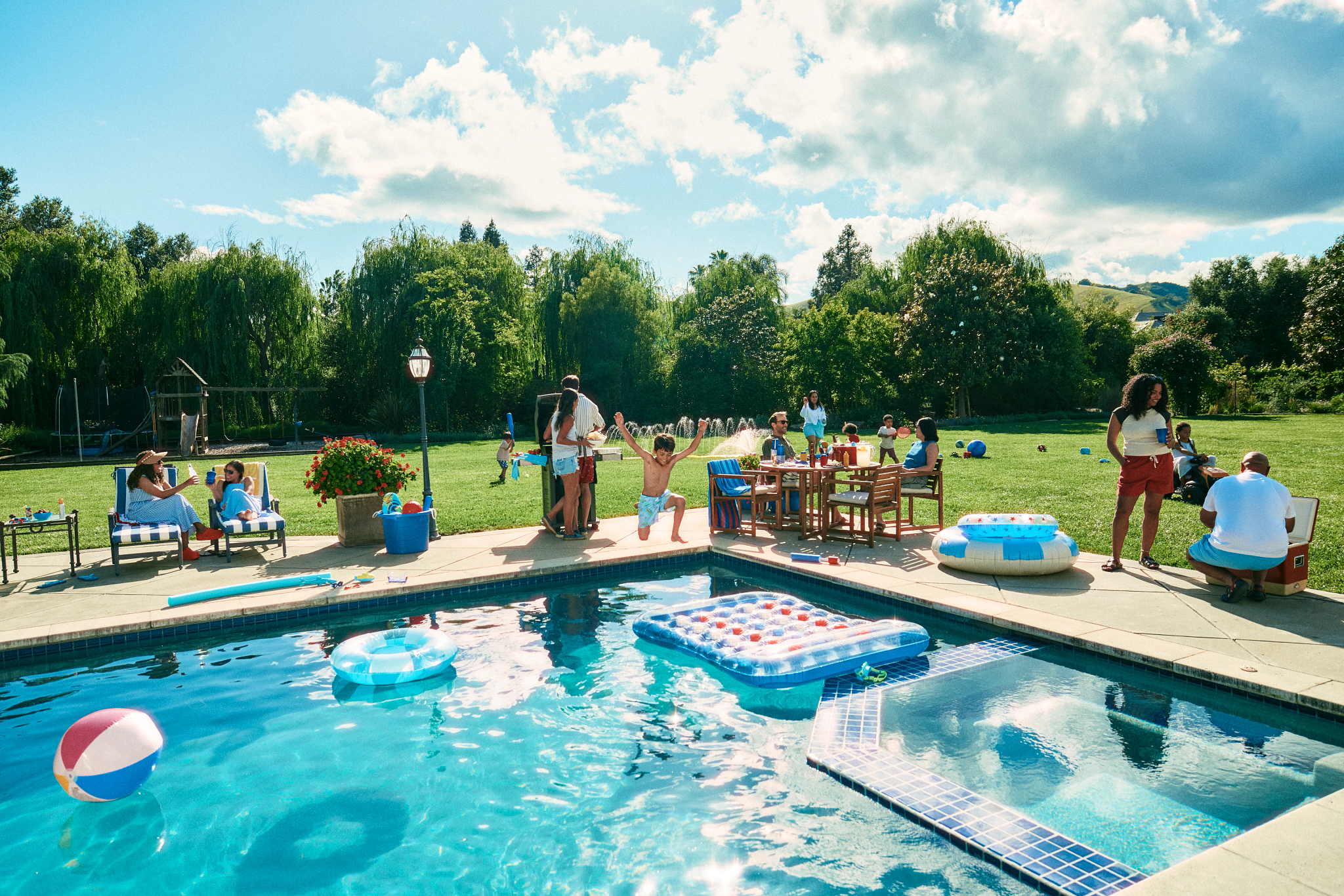 A family enjoying a sunny summer pool party in a spacious green backyard with a sparkling swimming pool.