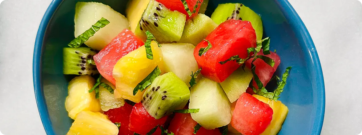 Top-down view of a blue bowl filled with diced watermelon, cantaloupe, kiwi, and pineapple tossed with fresh chopped mint.