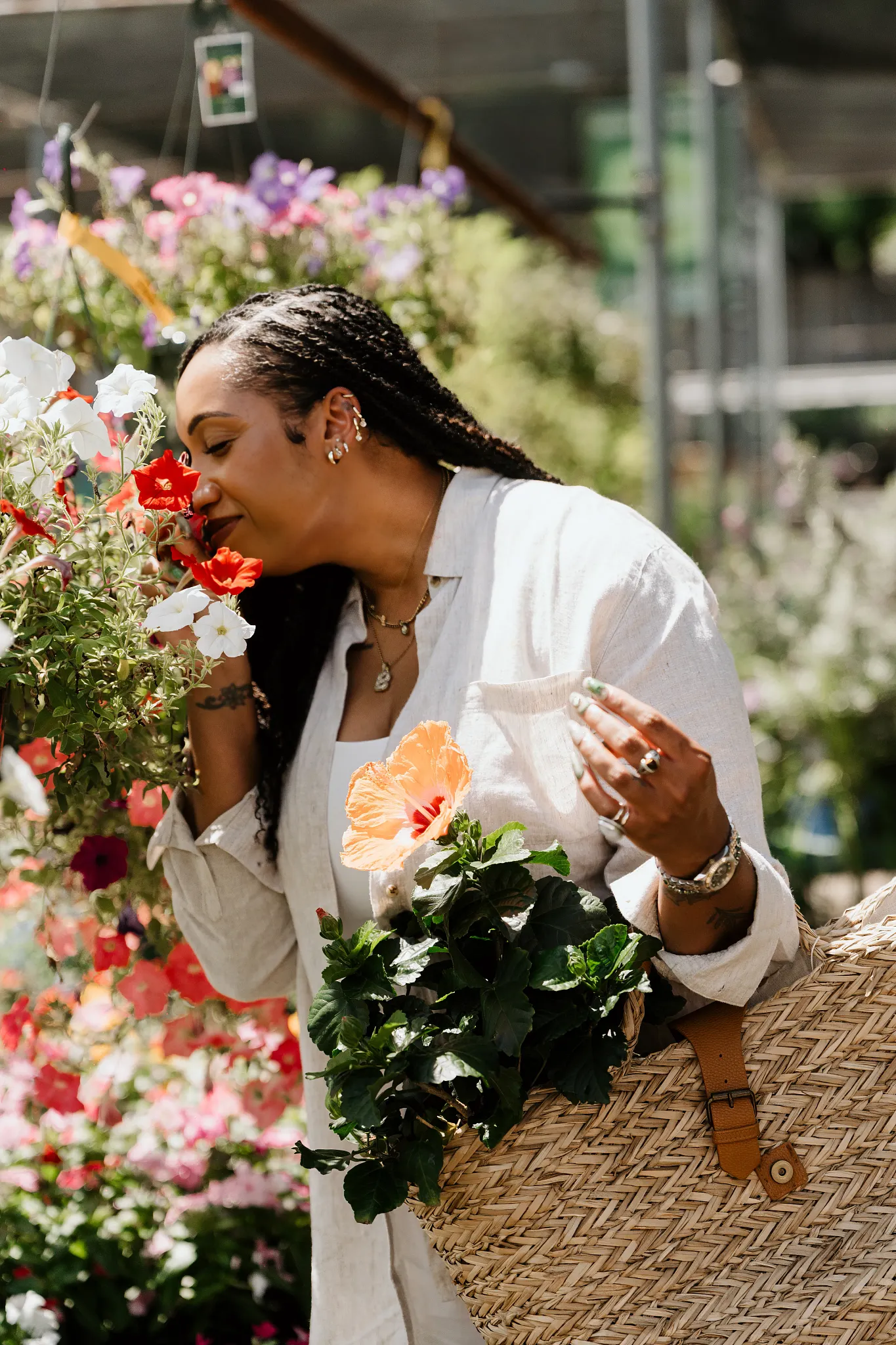 Britt smelling flowers from a hanging basket when walking through the plant store with a hibiscus plant popping out of her purse