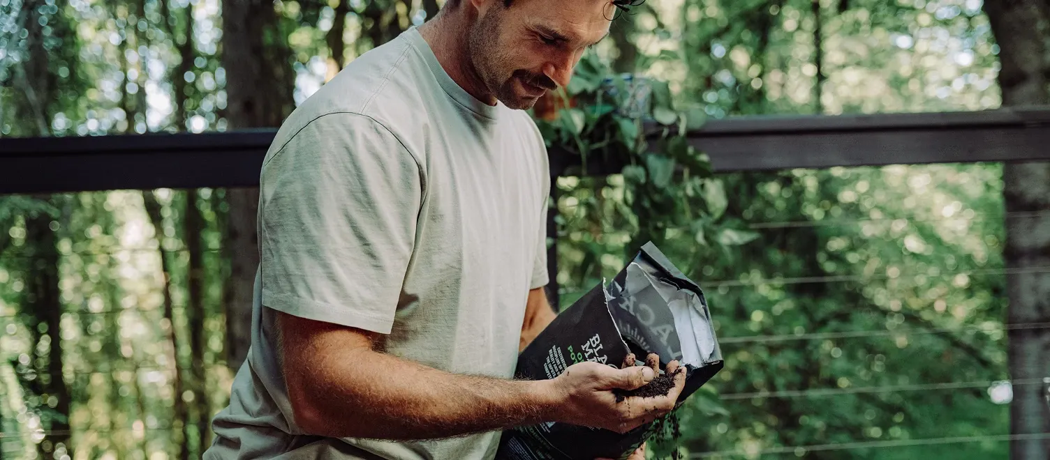 Person holding a bag of Black Magic Potting Soil in one hand and raw soil in the other hand.