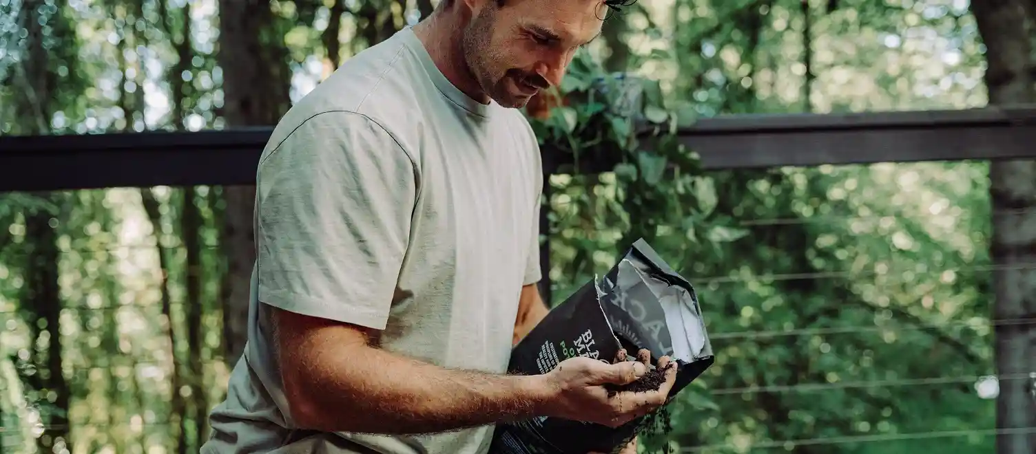 Person holding a bag of Black Magic Potting Soil in one hand and raw soil in the other hand.
