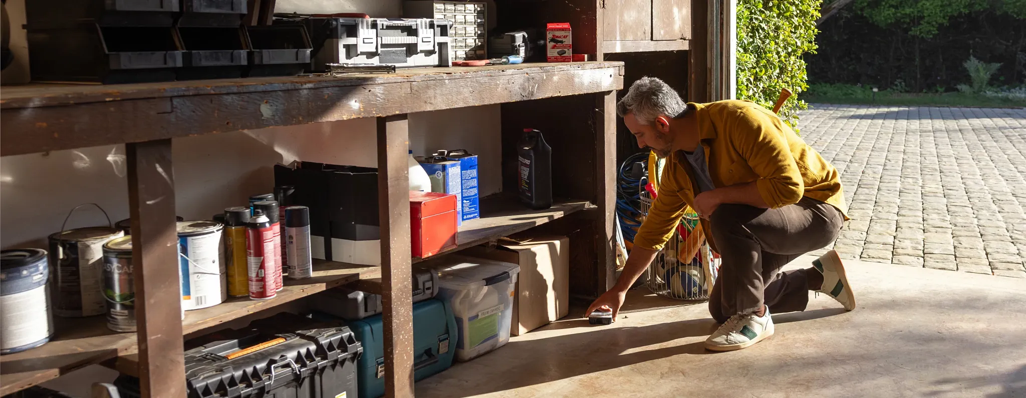 A man kneeling down to put a trap under his workbench in his garage