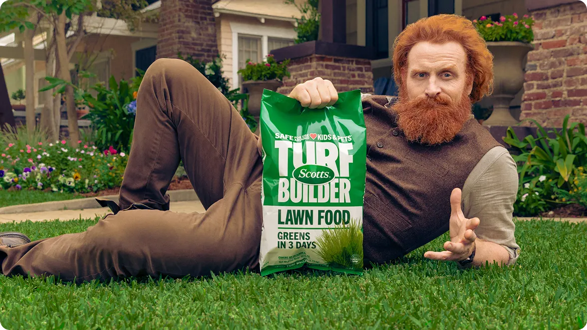 A man holding Scotts Turf Builder Lawn Food on green grass, inviting users to build a custom year-round lawn feeding plan