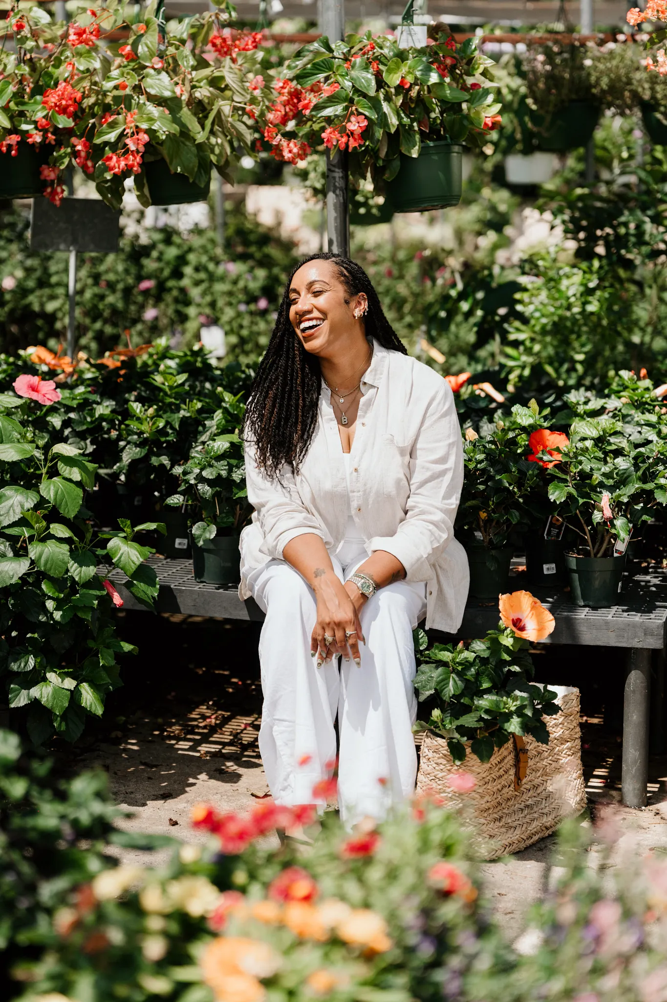 Britt sitting on a bench at the plant shop surrounded by blooming plants