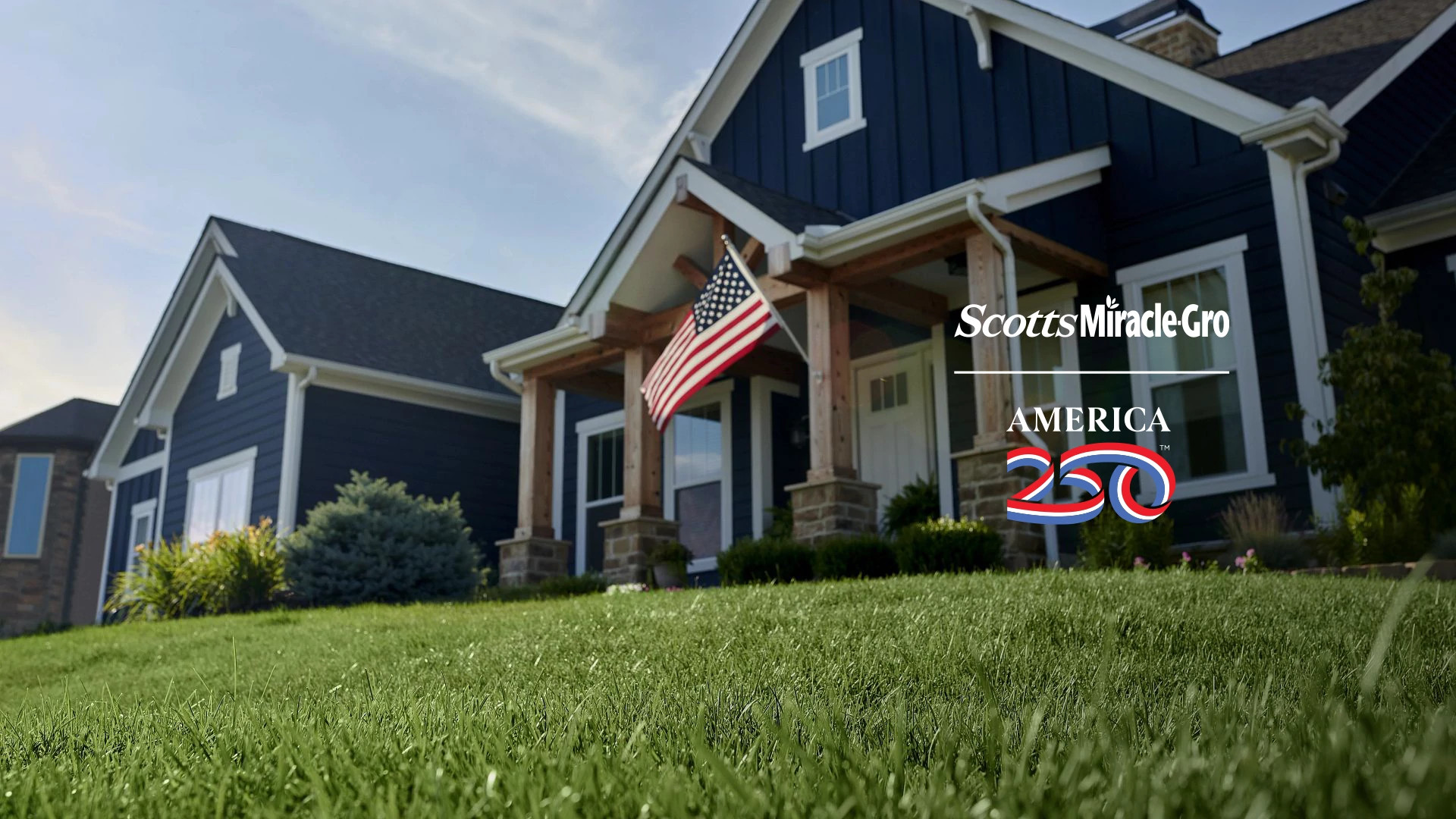 green grass and a blue modern farmhouse with a U.S. flag
